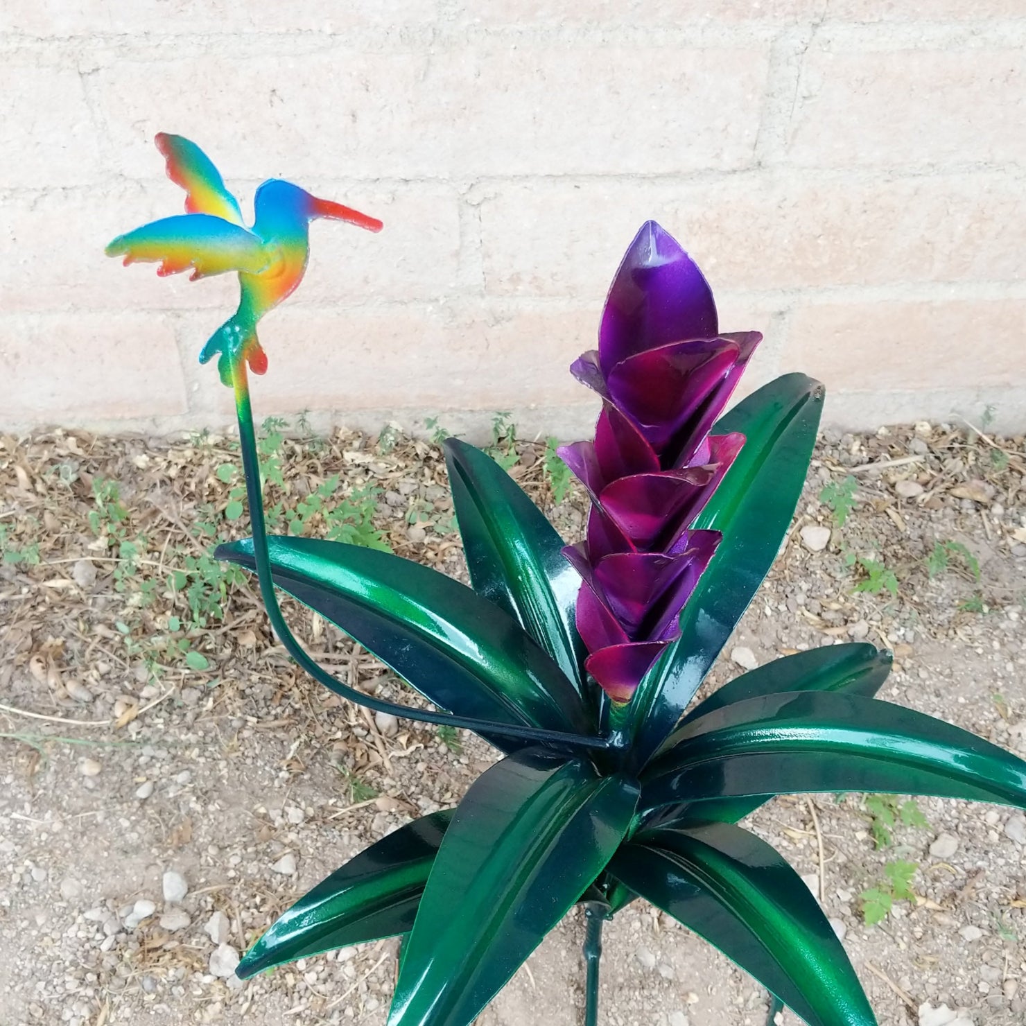 A large purple metal flower and a multicolor hummingbird.
