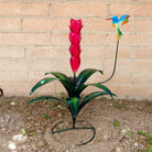 A red metal flower with green leaves and a multicolored hummingbird perched above.
