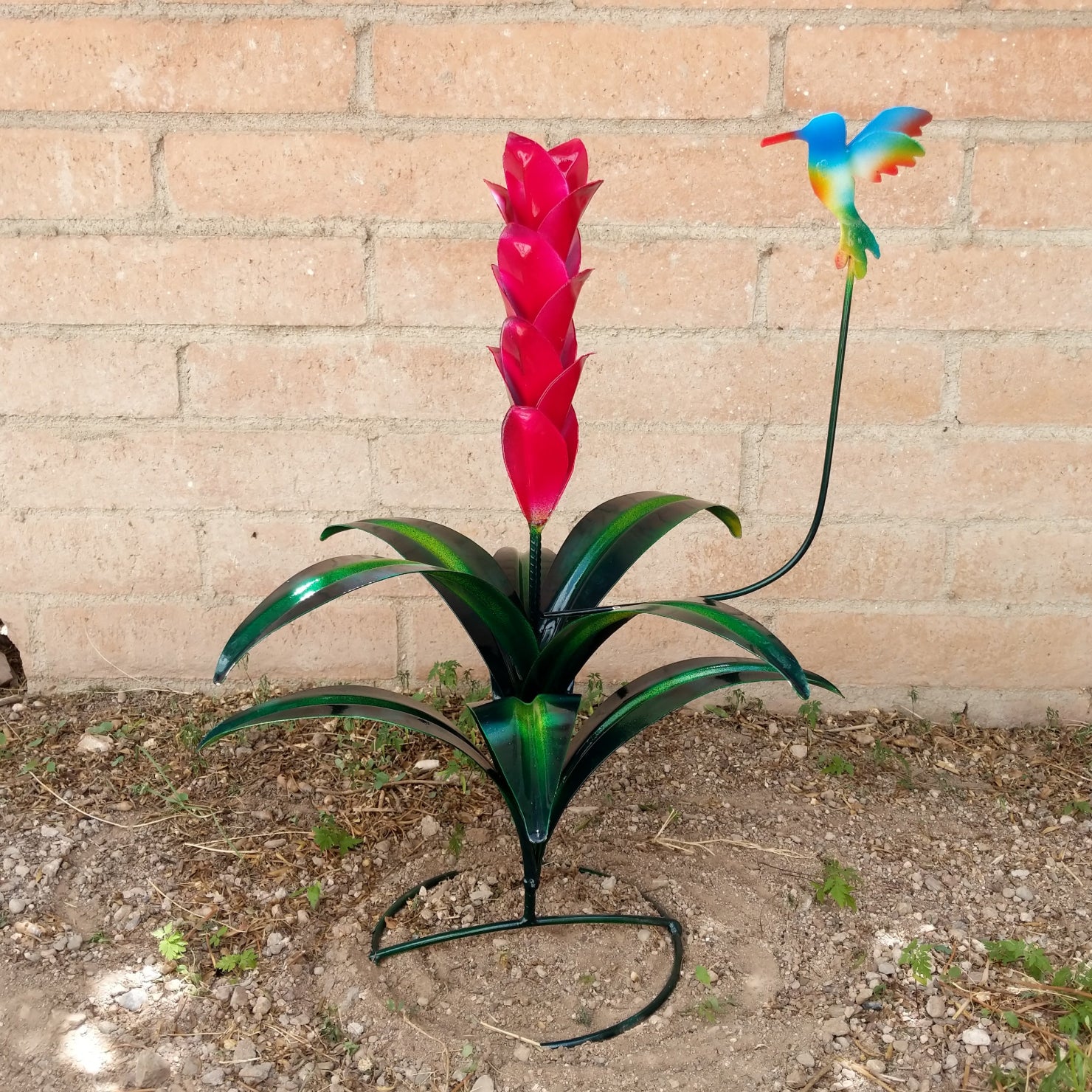 A red metal flower with green leaves and a multicolored hummingbird perched above.