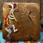 This Crooks Design metal clock features a silver-toned flute-playing Kokopelli with red and yellow Sunset Swirl accents, cutout hour markers, black clock hands, and a warm textured metal background.