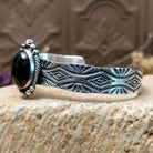 Sterling silver cuff bracelet with black onyx set in the oval bezel, framed by twisted rope and dotted accents while the band features abstract stamping.