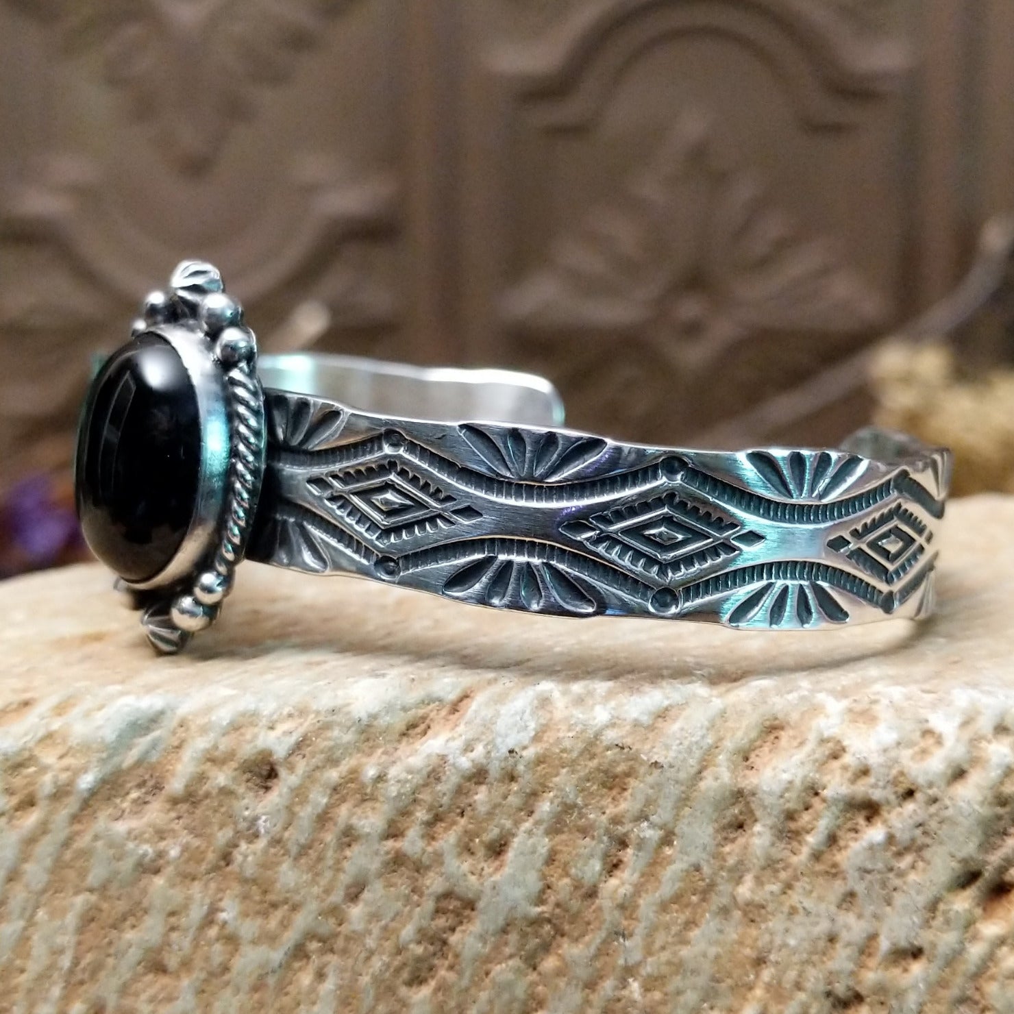 Sterling silver cuff bracelet with black onyx set in the oval bezel, framed by twisted rope and dotted accents while the band features abstract stamping.