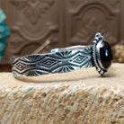 Sterling silver cuff bracelet with black onyx set in the oval bezel, framed by twisted rope and dotted accents while the band features abstract stamping.