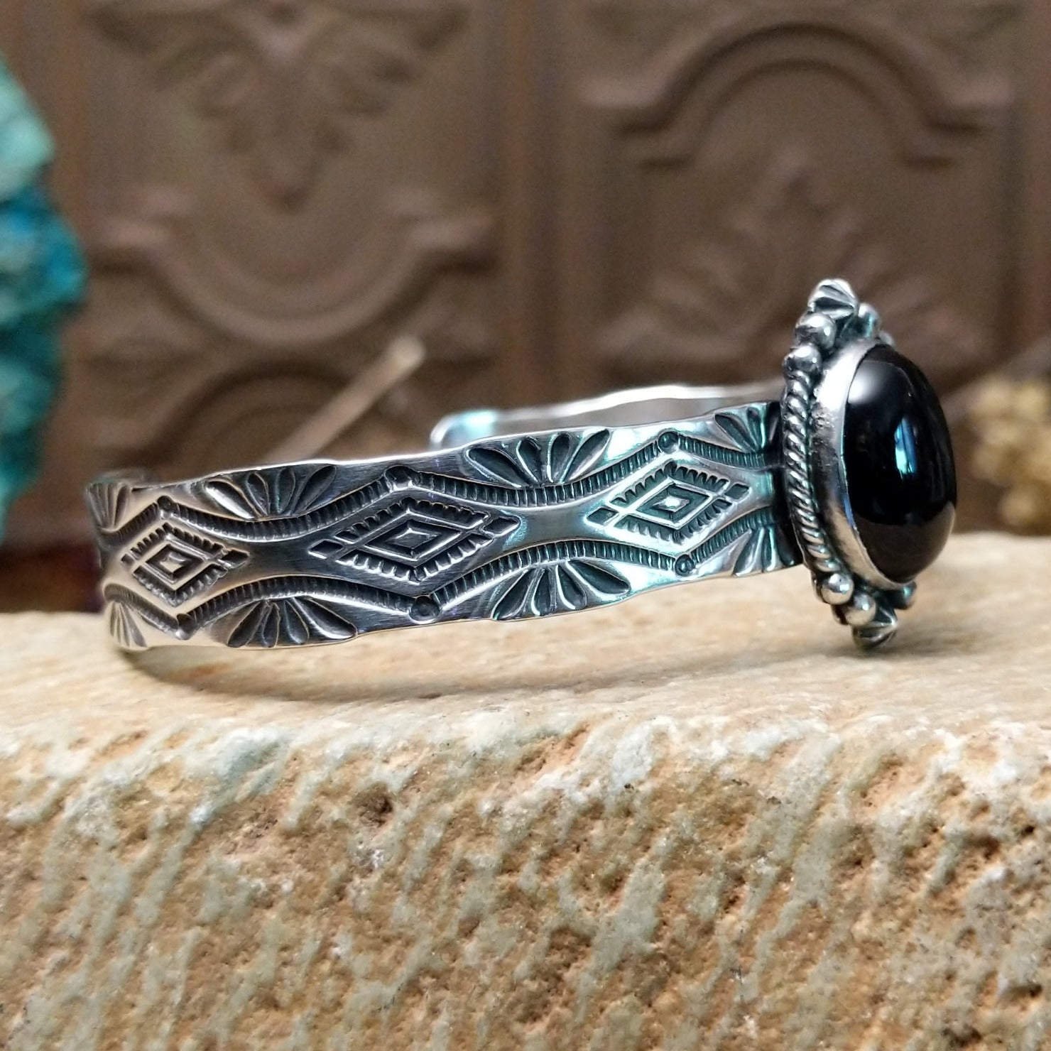 Sterling silver cuff bracelet with black onyx set in the oval bezel, framed by twisted rope and dotted accents while the band features abstract stamping.