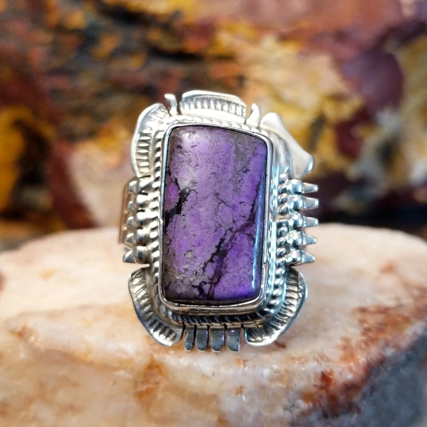 Square sugilite ring set within an intricate silver work bezel.