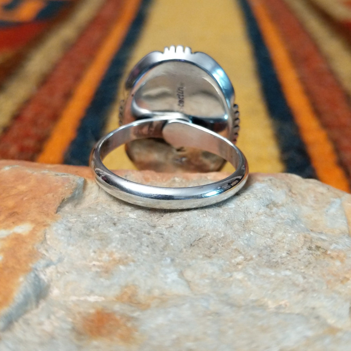 This distinctive White Buffalo Ring by Alfred Martinez features a large oval white stone with black matrix patterns, surrounded by a silver rope border and decorative stamped silver setting; underside view.