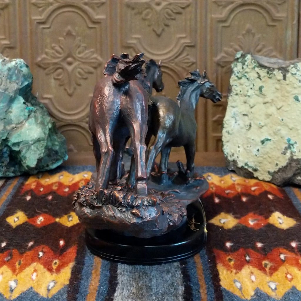 Sculpture showing three bronze-colored horses galloping with flowing manes on a textured base.