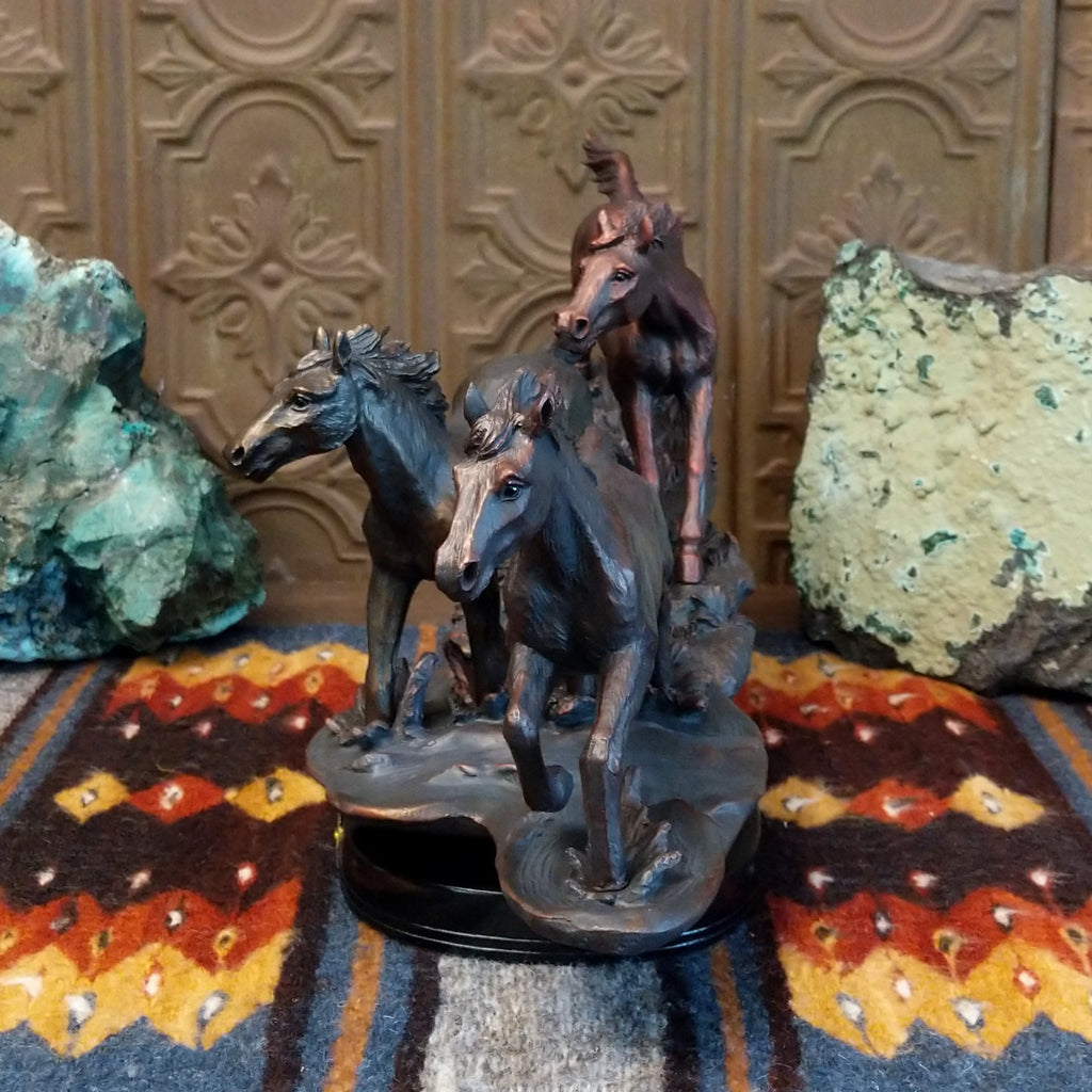 Sculpture showing three bronze-colored horses galloping with flowing manes on a textured base.