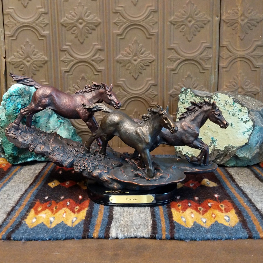 Sculpture showing three bronze-colored horses galloping with flowing manes on a textured base.