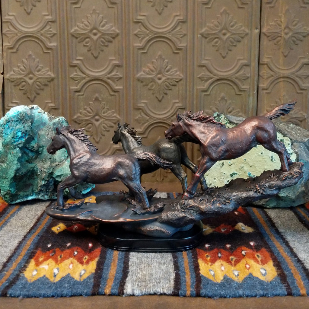 Sculpture showing three bronze-colored horses galloping with flowing manes on a textured base.