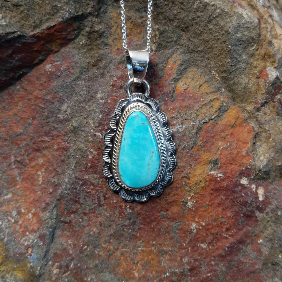 Turquoise pendant by Burt Francisco featuring a large teardrop-shaped blue turquoise stone surrounded by twisted rope and scalloped sterling silverwork.