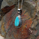 Turquoise pendant by Burt Francisco featuring a large teardrop-shaped blue turquoise stone surrounded by twisted rope and scalloped sterling silverwork; side view.
