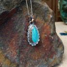 Turquoise pendant by Burt Francisco featuring a large teardrop-shaped blue turquoise stone surrounded by twisted rope and scalloped sterling silverwork; side view.