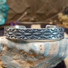 Sterling silver cuff bracelet with stamped designs on the surface.