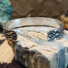 Sterling silver cuff bracelet with stamped designs on the surface.