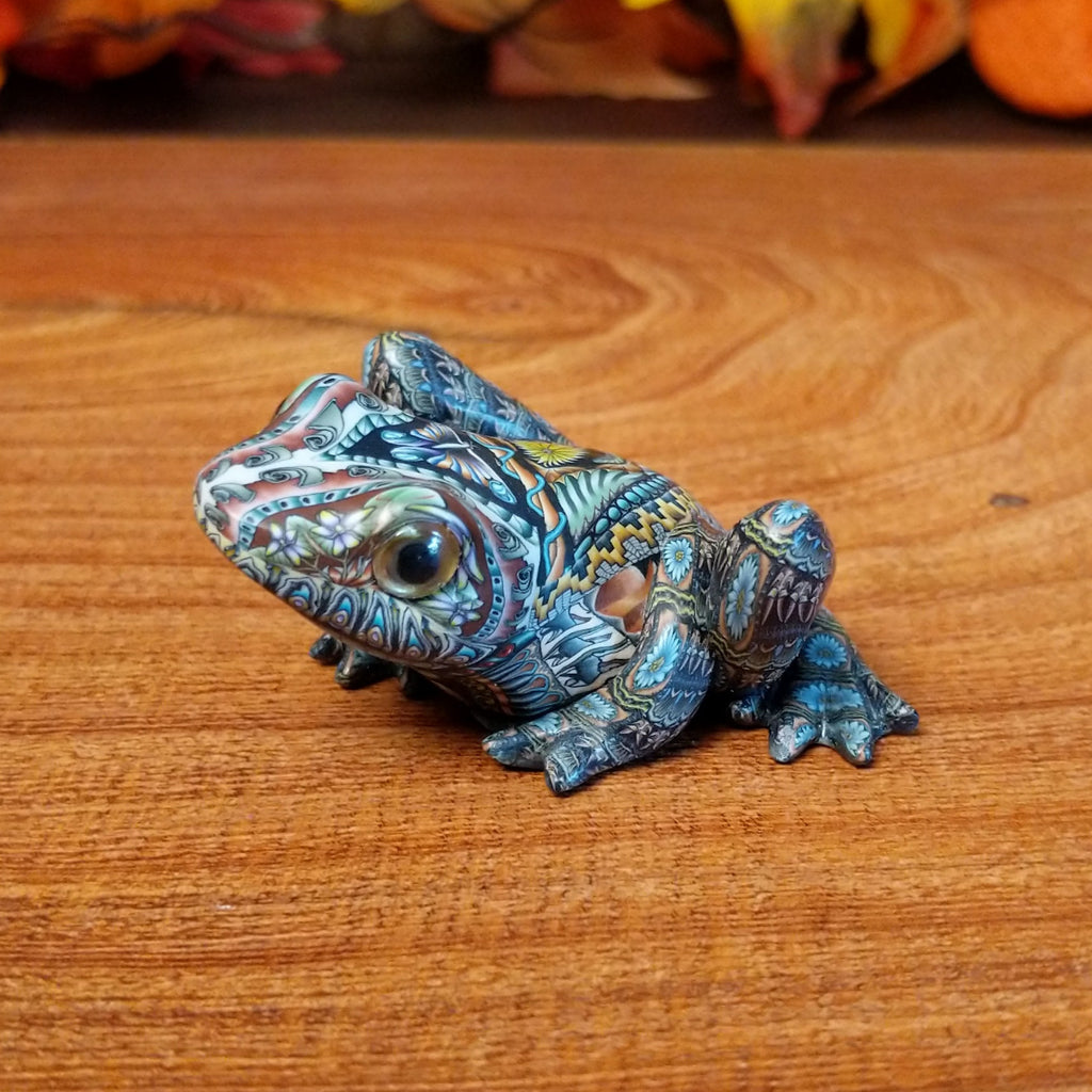 Polymer clay shaped into a frog with intricate designs and vibrant colors on the body.