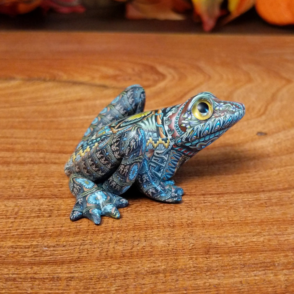 Polymer clay shaped into a frog with intricate designs and vibrant colors on the body.