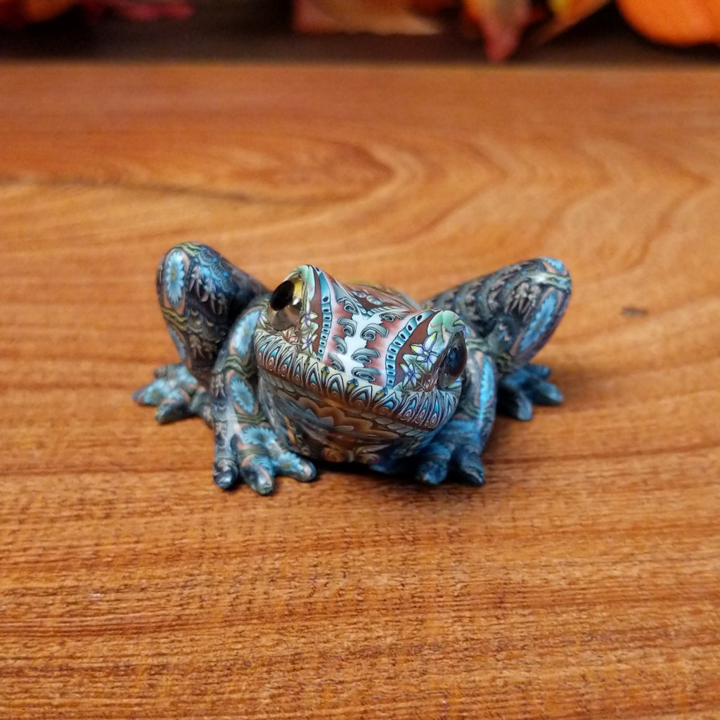 Polymer clay shaped into a frog with intricate designs and vibrant colors on the body.