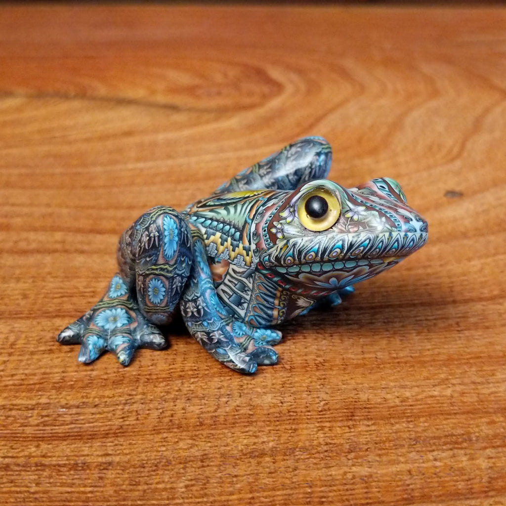 Polymer clay shaped into a frog with intricate designs and vibrant colors on the body.