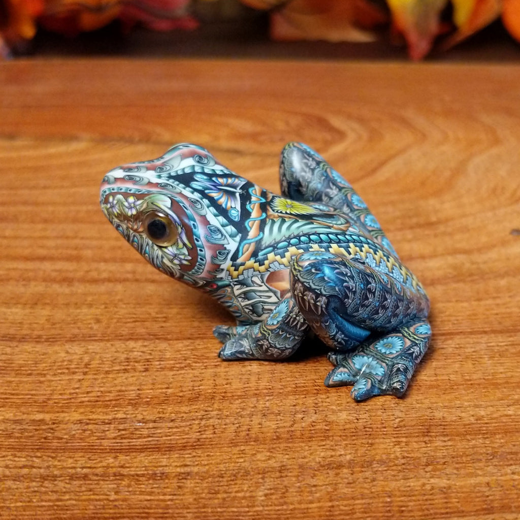 Polymer clay shaped into a frog with intricate designs and vibrant colors on the body.