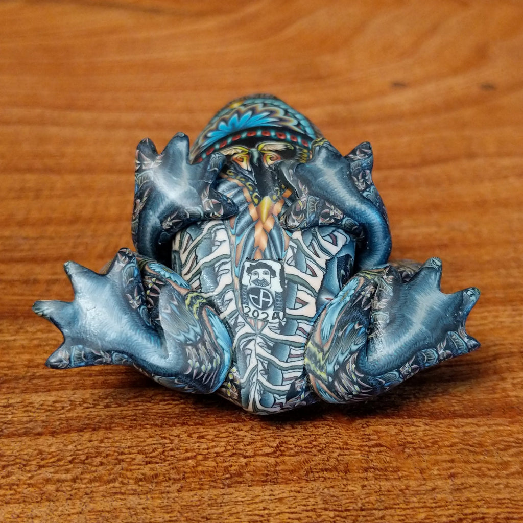 Polymer clay shaped into a frog with intricate designs and vibrant colors on the body with its made in "2024" design.