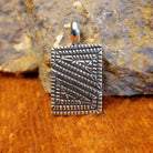 Square sterling silver pendant with geometric designs stamped on the surface.