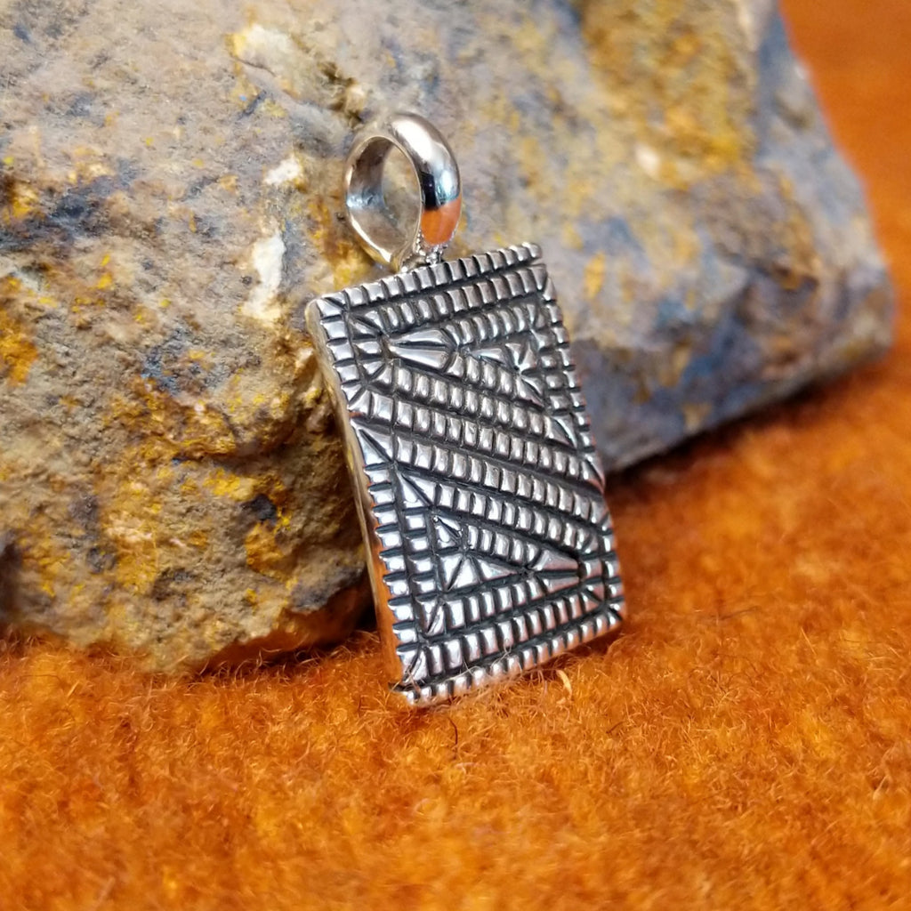 Square sterling silver pendant with geometric designs stamped on the surface.