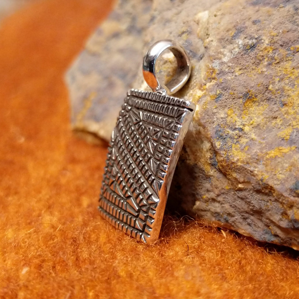 Square sterling silver pendant with geometric designs stamped on the surface.