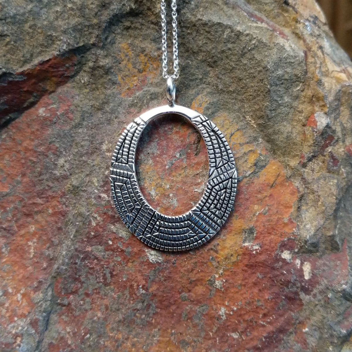 Geometric spiral silver pendant by Elgin Tom featuring an open oval design with intricate stamped patterns, polished silver, and dark oxidized detailing.