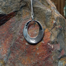 Geometric spiral silver pendant by Elgin Tom featuring an open oval design with intricate stamped patterns, polished silver, and dark oxidized detailing; artisan and Sterling Silver stamp.