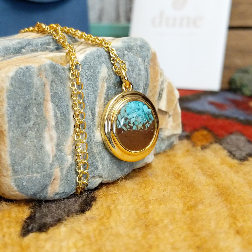Round necklace pendant with a gold-plated brass frame, filled with a vibrant turquoise and sand.