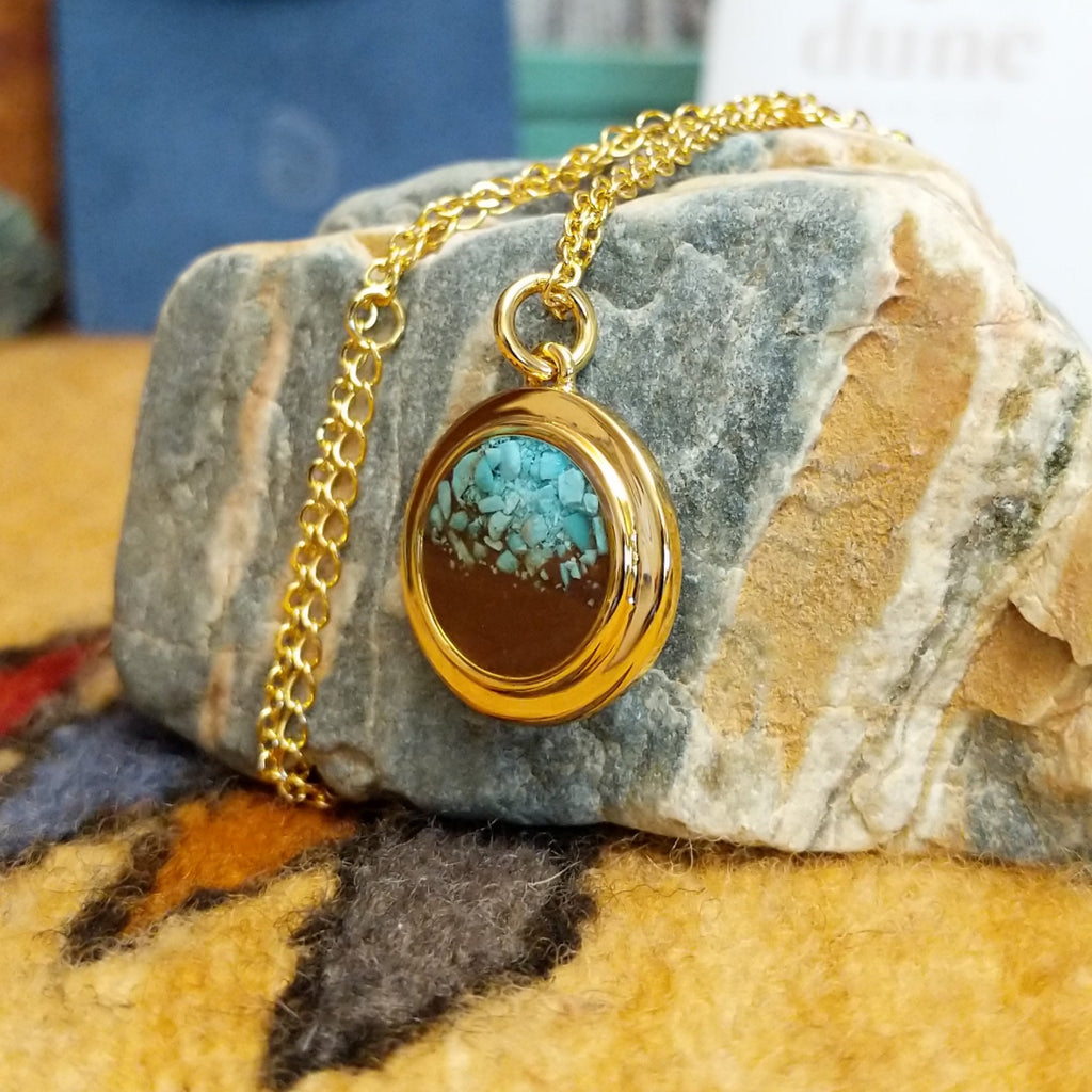 Round necklace pendant with a gold-plated brass frame, filled with a vibrant turquoise and sand.