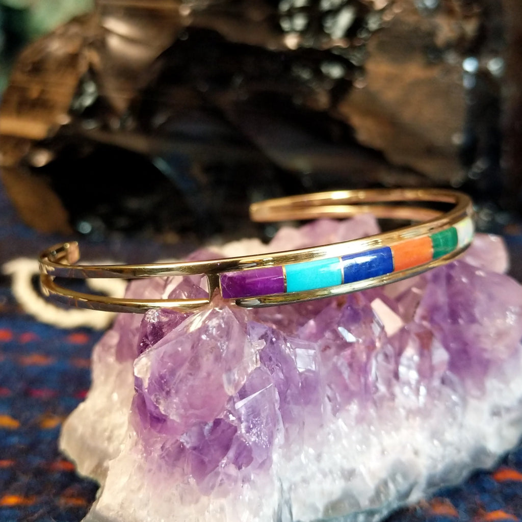  Gold cuff bracelet featuring a vibrant, multi-stone inlay set in a polished gold frame.