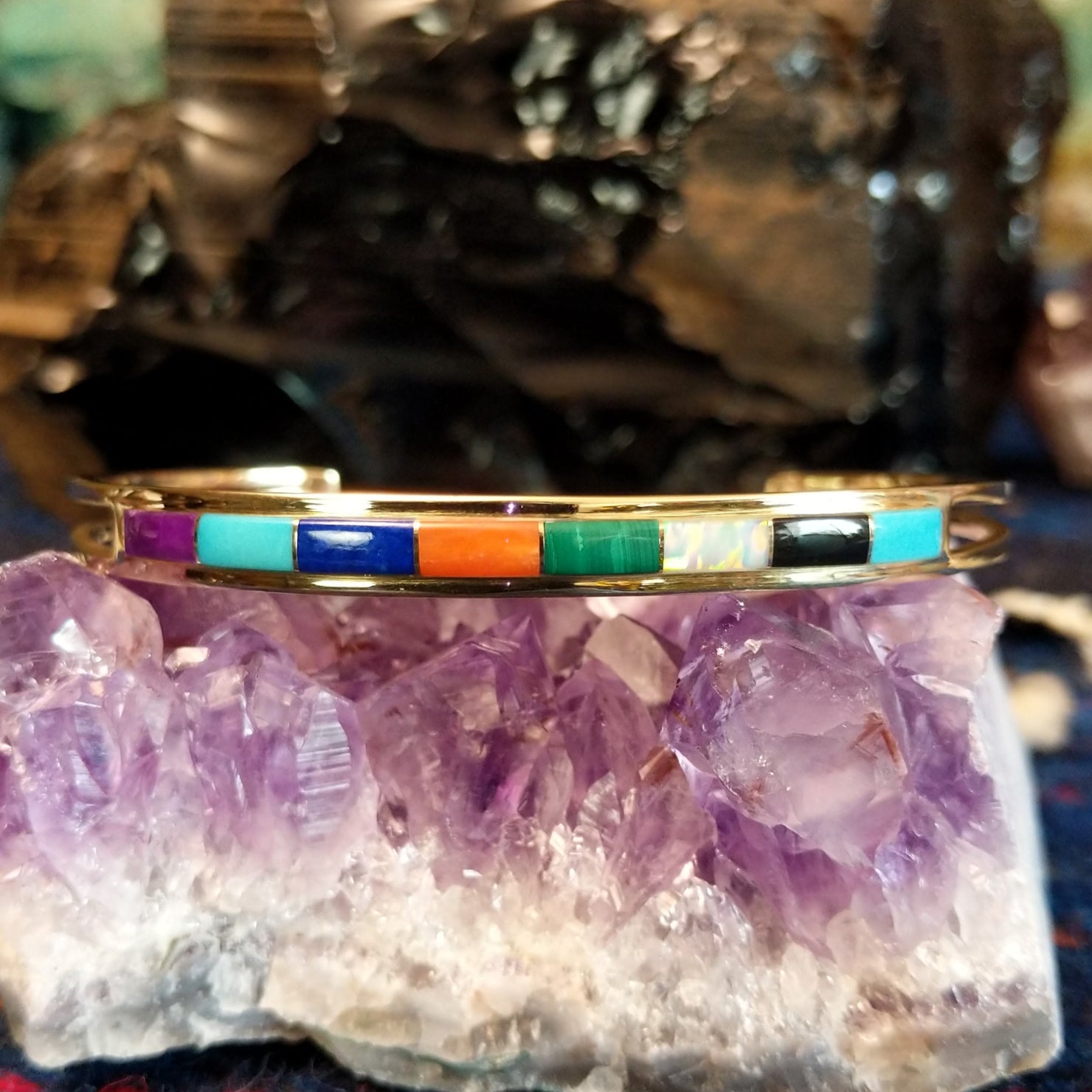  Gold cuff bracelet featuring a vibrant, multi-stone inlay set in a polished gold frame.