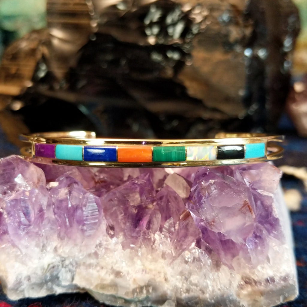  Gold cuff bracelet featuring a vibrant, multi-stone inlay set in a polished gold frame.