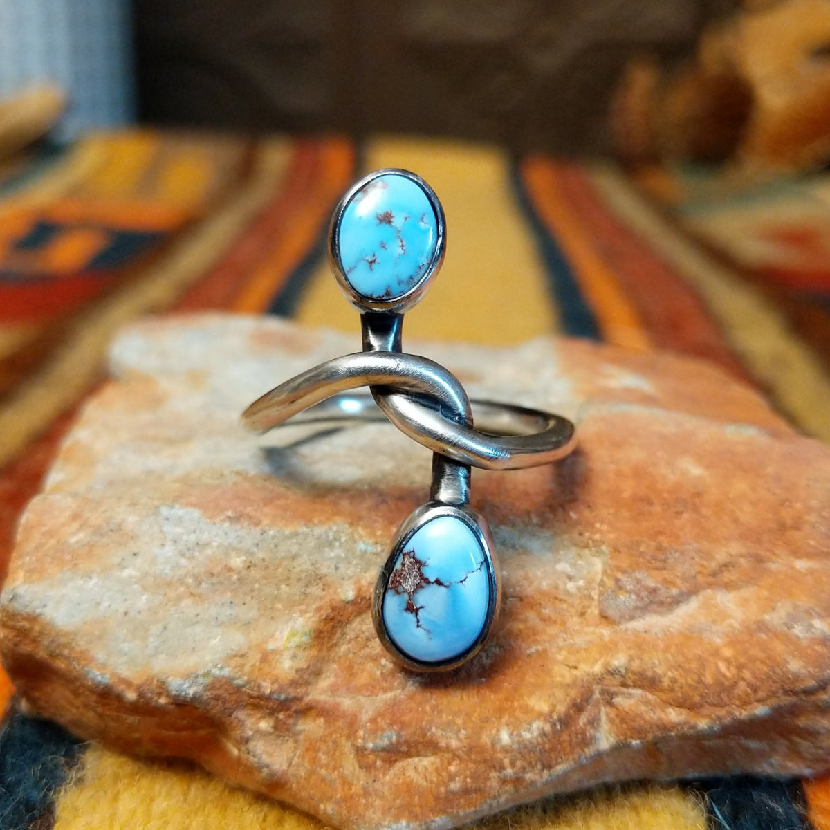 Golden Hills Turquoise Ring by Raymond Coriz featuring two oval light blue turquoise stones with natural matrix, set at opposite ends of a polished silver band with an elegant, flowing design.