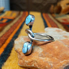 Golden Hills Turquoise Ring by Raymond Coriz featuring two oval light blue turquoise stones with natural matrix, set at opposite ends of a polished silver band with an elegant, flowing design; side view.