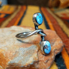 Golden Hills Turquoise Ring by Raymond Coriz featuring two oval light blue turquoise stones with natural matrix, set at opposite ends of a polished silver band with an elegant, flowing design; side view.