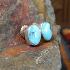 A side view of the golden hills turquoise oval earrings by Diane Wylie shows the turquoise stone’s smooth edge in a simple bezel. The silver post gleams against the stone’s bright blue hue.