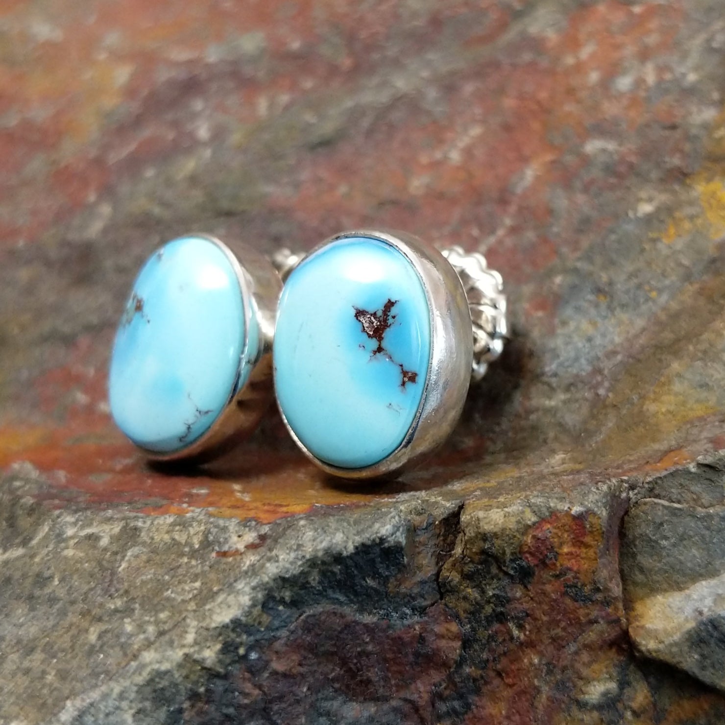 A side view of the golden hills turquoise oval earrings by Diane Wylie shows the turquoise stone’s smooth edge in a simple bezel. The silver post gleams against the stone’s bright blue hue.