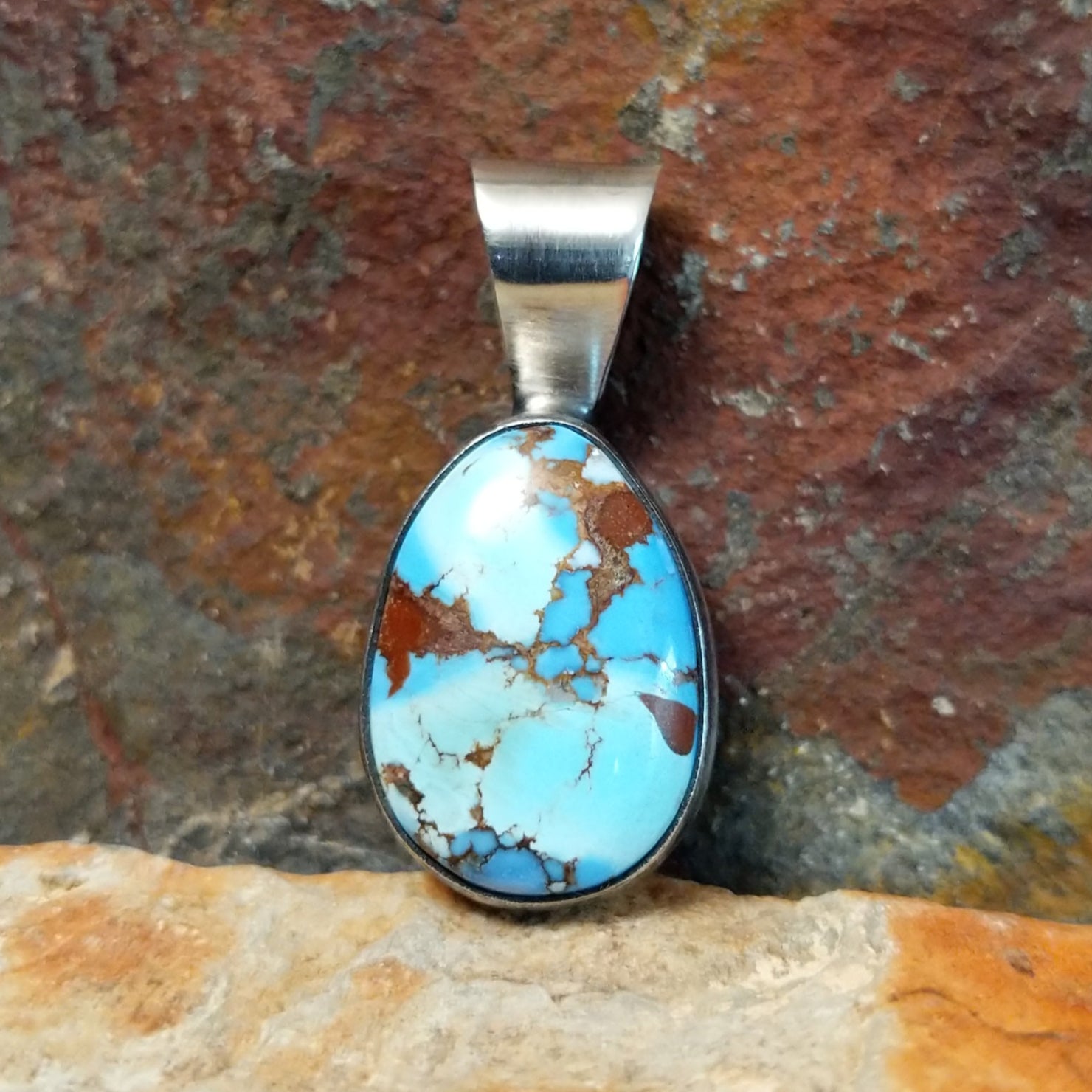 A Navajo-crafted pendant features an oval golden hills turquoise stone with dark brown matrix in a smooth silver bezel.