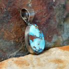 The side of this turquoise pendant shows a polished silver base with a sleek bail at the top.