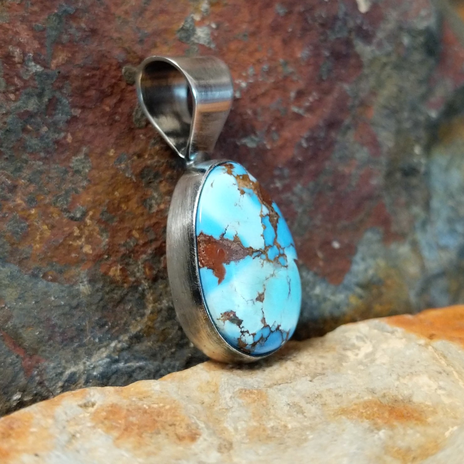 The side of this turquoise pendant shows a polished silver base with a sleek bail at the top.