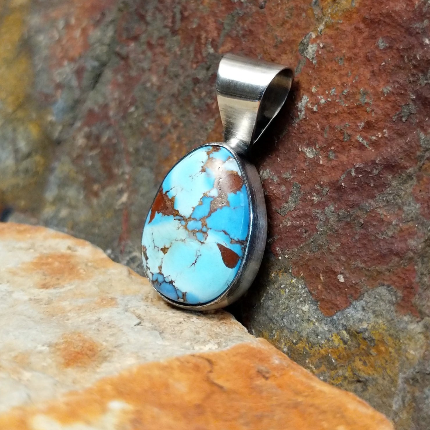The side of this turquoise pendant shows a polished silver base with a sleek bail at the top.