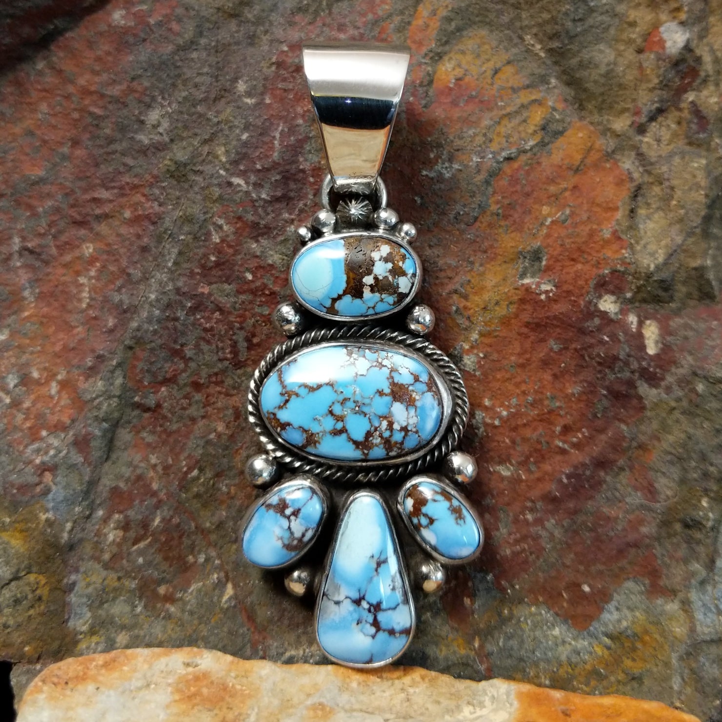 A Southwest Native American pendant glows with five vibrant turquoise stones, their brown matrix striking against simple silver bezels and a twisted rope design. Small silver beads add delicate charm between the stones.