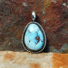 A Navajo-crafted pendant features an oval golden hills turquoise stone with dark brown matrix in a twisted silver bezel.