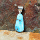 A Navajo-crafted pendant features a teardrop-shaped golden hills turquoise stone with dark brown matrix in a smooth silver bezel.