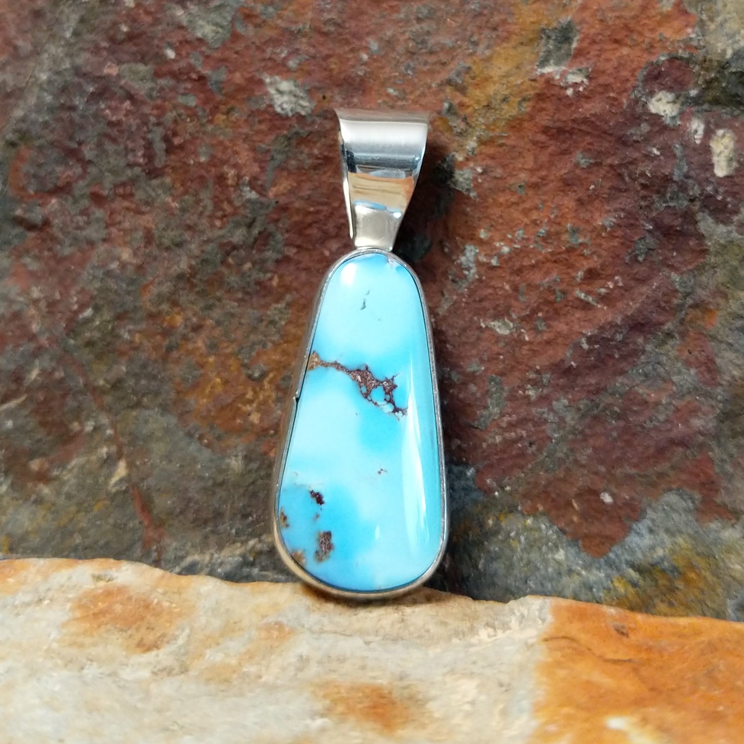A Navajo-crafted pendant features a teardrop-shaped golden hills turquoise stone with dark brown matrix in a smooth silver bezel.