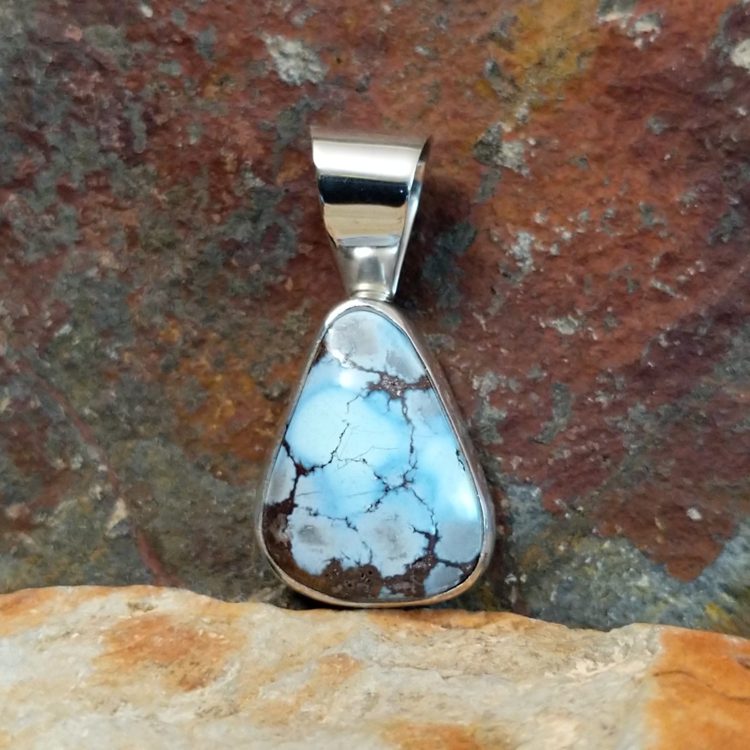 A sterling silver pendant features a triangular Golden Hills turquoise stone in a smooth bezel.