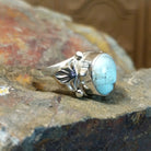 Silver ring with a smooth bezel holding a round turquoise stone with silver accents along the bezel and band.